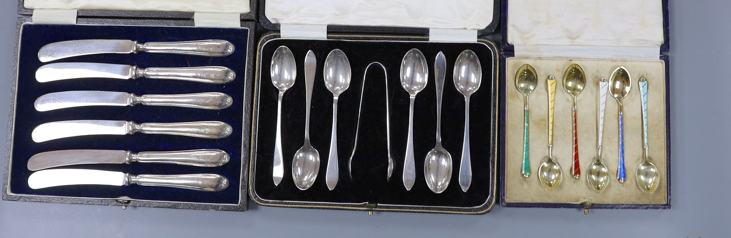 A cased set of six Danish gilt sterling and polychrome enamel coffee spoons, a cased set of six silver teaspoons with tongs and a cased set of six silver handled tea knives.